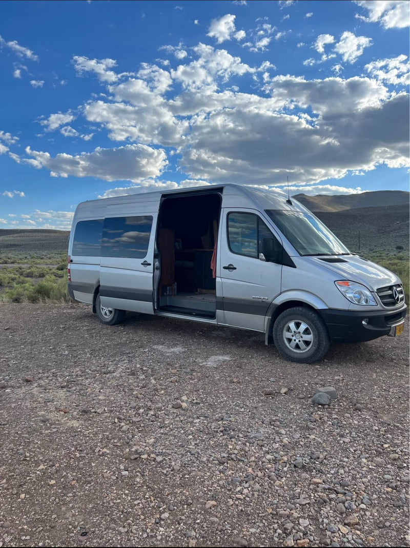  and a fold-down table. A basket with a blanket sits below.|Scenic RV rental adventure: cozy bed setup with a stunning sunset over the landscape — photo 3