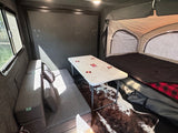 Inside a versatile **rv rental**: compact living space with folding table, couch/bed, and pop-up tent sleeping area.