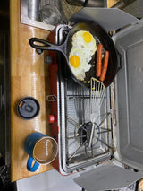 RV rental breakfast: Fried eggs & sausages cooking on a portable stove, with a coffee mug on a wooden counter.