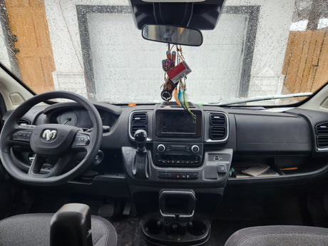 Inside a modern rv rental van: rainy windshield view, Ram dashboard with steering wheel, infotainment, and gear shift.