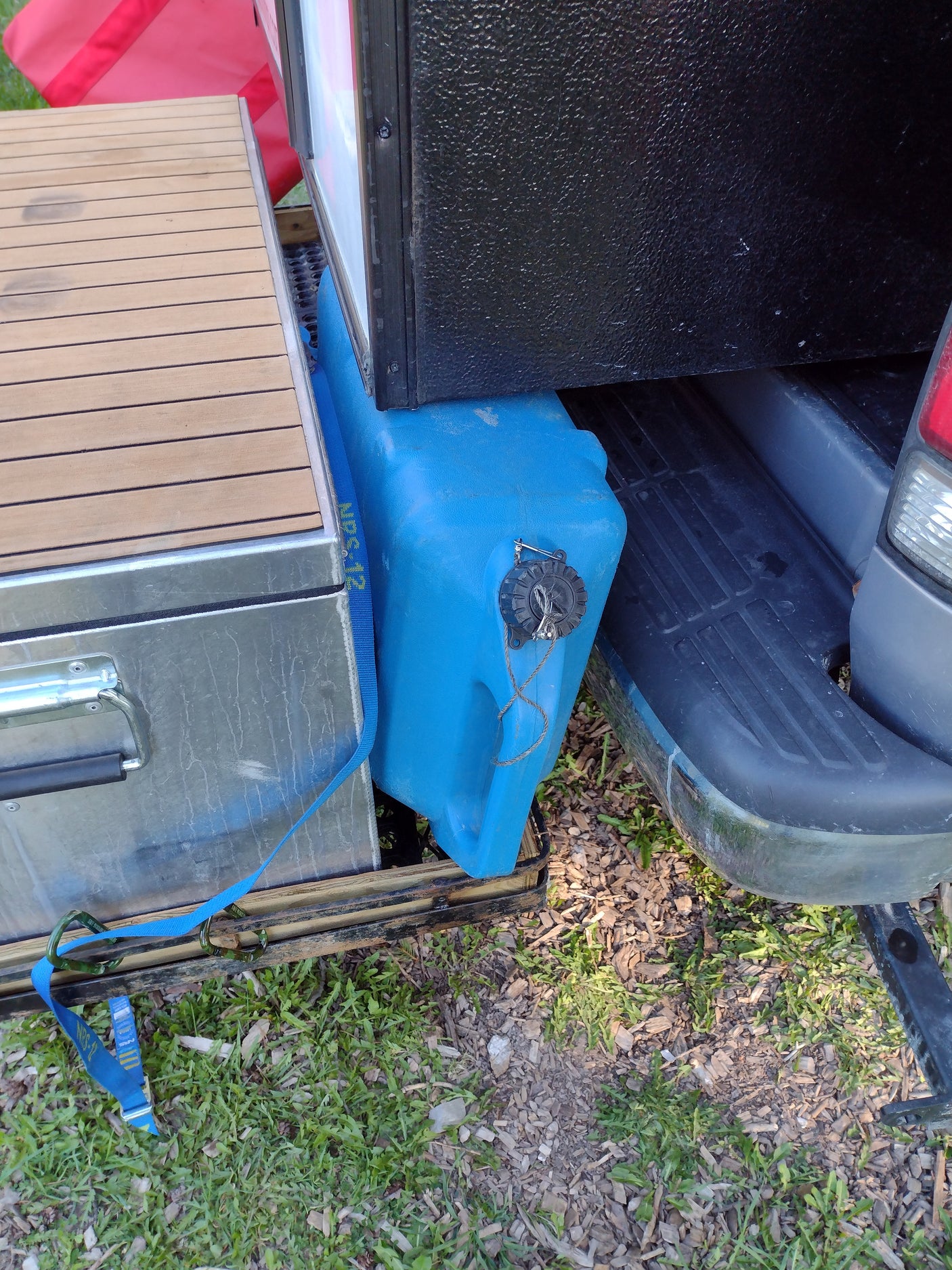 RV rental outdoor gear: Blue water tank & wood-topped storage box securely strapped on a vehicle's rear carrier.