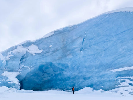 An adventurer stands before a colossal blue glacier, surrounded by snow. Experience such grandeur with an RV rental!