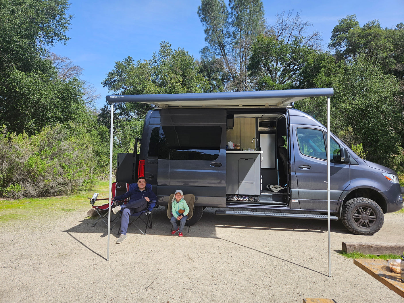Relaxing outdoors with a modern RV rental, featuring an extended awning and full kitchenette for family camping.