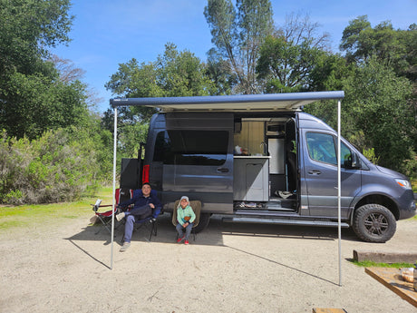 Relaxing outdoors with a modern RV rental, featuring an extended awning and full kitchenette for family camping.