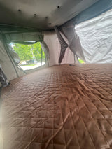 View from inside an RV rental rooftop tent, featuring a quilted mattress and outdoor street view.
