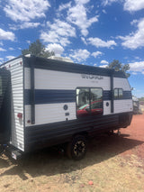 Side view of a Wolf Pup travel trailer parked under a bright blue sky with white clouds. Perfect for an RV rental adventure.