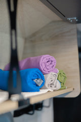 Colorful, rolled towels neatly arranged on a wooden shelf inside an RV rental, providing home-like comfort.