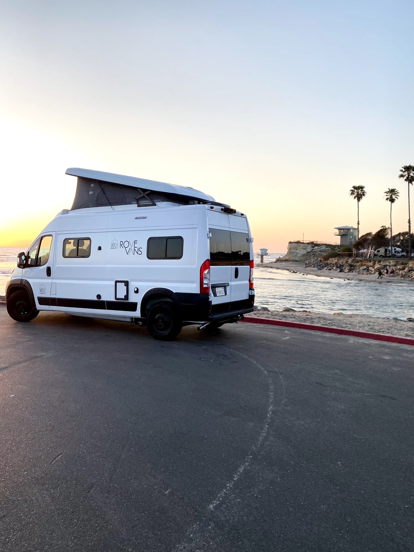 A white Rove Vans camper van rental, with its pop-top extended, parked beachfront at sunset for a perfect RV adventure.