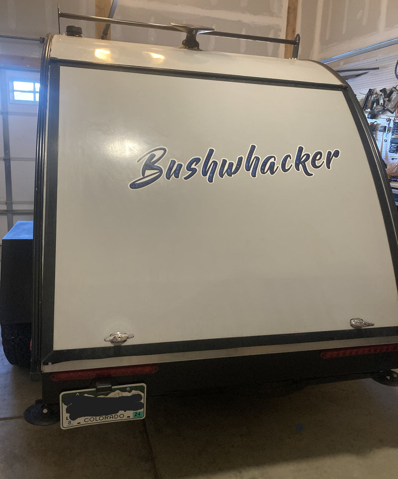 Rear of a white Bushwhacker travel trailer (RV rental option) in a garage, with a roof rack & Colorado plate. — photo 12