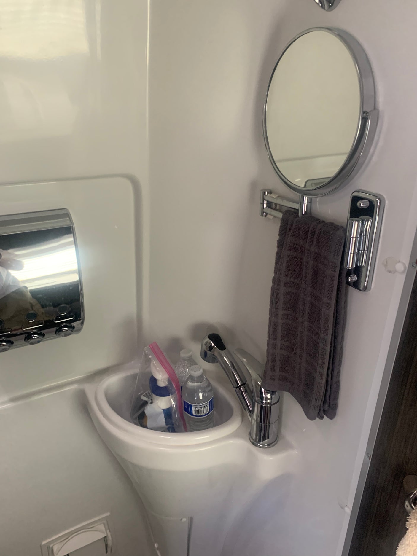 Inside an RV rental, a compact white bathroom features a sink, chrome faucet, mirror, and towel. Water bottles and toiletries are visible.