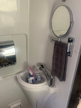Inside an RV rental, a compact white bathroom features a sink, chrome faucet, mirror, and towel. Water bottles and toiletries are visible.