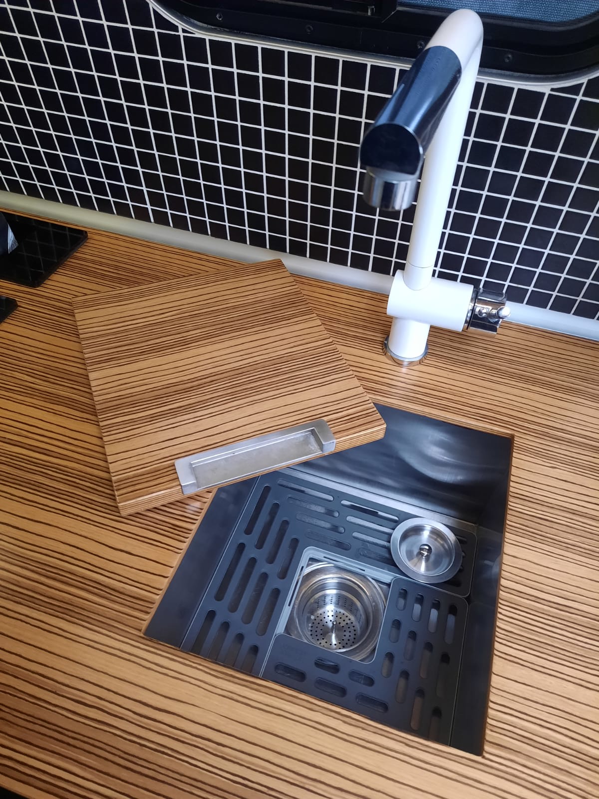 RV rental kitchen features: striped counter, grid backsplash, white faucet, and a black sink with a versatile wooden cover/board. — photo 18