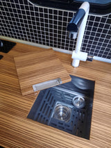 RV rental kitchen features: striped counter, grid backsplash, white faucet, and a black sink with a versatile wooden cover/board.