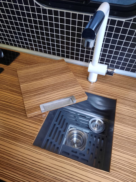 RV rental kitchen features: striped counter, grid backsplash, white faucet, and a black sink with a versatile wooden cover/board.