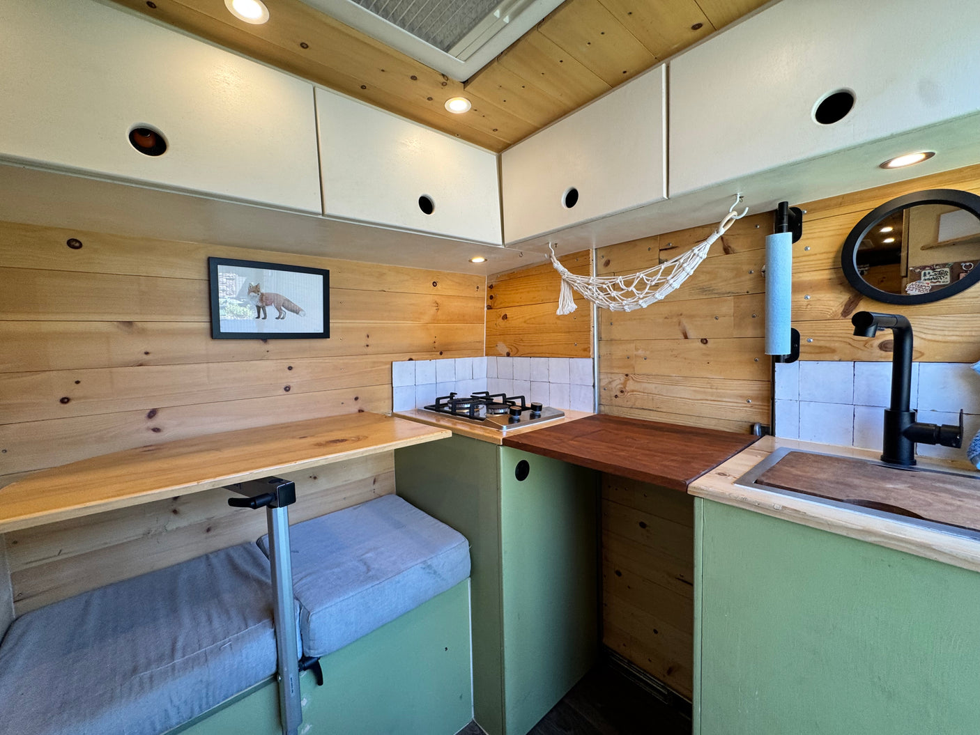 Cozy RV rental kitchen: wooden walls, stove, sink, and flexible dining area. Perfect for compact living.