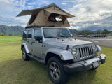 Silver Jeep Wrangler with a rooftop tent on green grass in Kauai. An ideal rv rental for outdoor adventures near mountains.