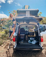 Adventure-ready RV rental! Woman on ladder accessing packed car with rooftop tent and gear for camping fun.