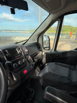 RV rental van interior, dashboard & wet windshield. View of a coastal scene with a person standing by the water.