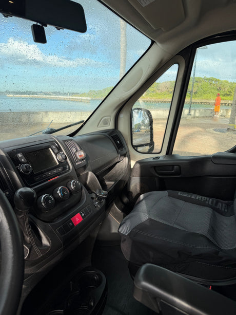 RV rental van interior, dashboard & wet windshield. View of a coastal scene with a person standing by the water.