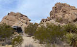 RV rental camper van parked at a scenic desert campsite, nestled among massive rock formations and native plants under a wide sky.
