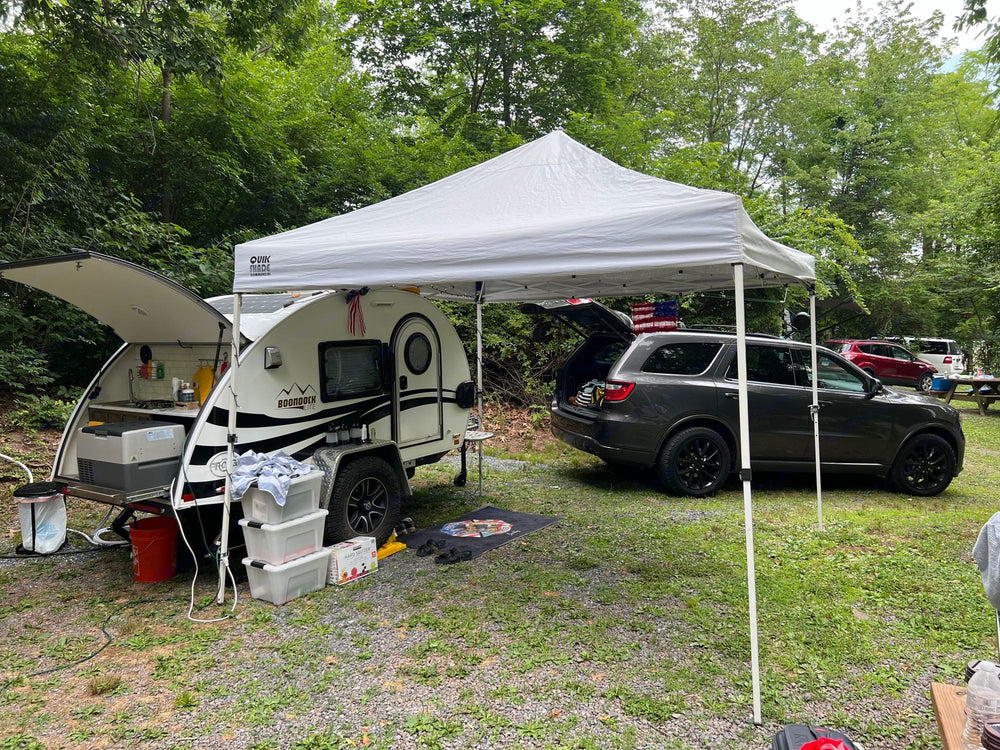  with chairs & pet bed.|White SUV towing a teardrop RV rental at a wooded campsite with gravel