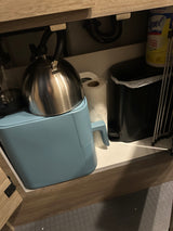 Under-sink storage in an RV rental, showing a kettle, paper towels, trash can, and Lysol wipes.