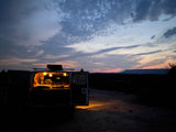 RV rental parked at dusk with illuminated interior and open doors, offering a view of a flat-topped mountain under a colorful sky.
