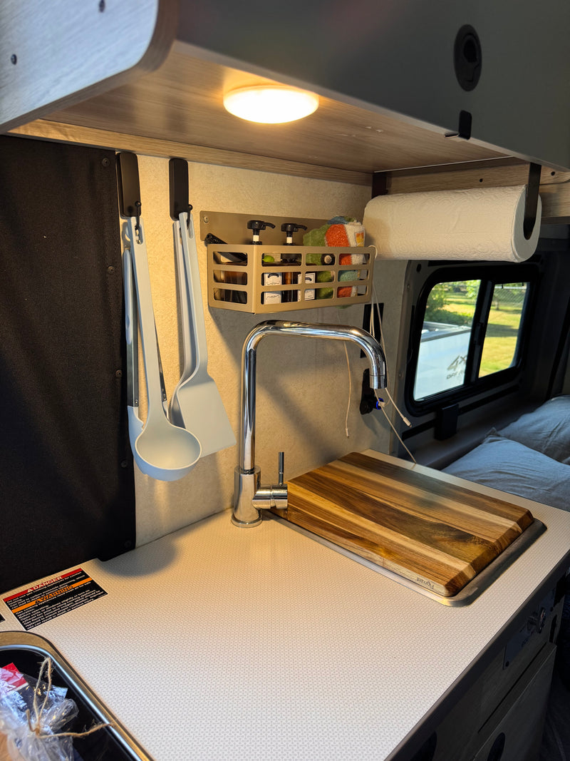 RV rental compact kitchen with chrome faucet, wooden cutting board, and organized hanging storage for cooking essentials. — photo 13