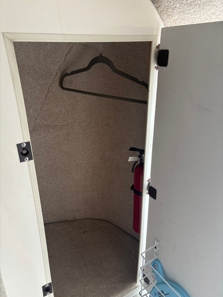 RV rental storage cabinet with a fire extinguisher, clothes hanger, and a white wire shelf on the door.