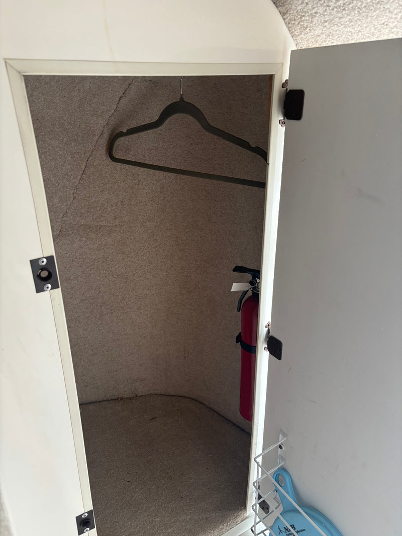 RV rental storage cabinet with a fire extinguisher, clothes hanger, and a white wire shelf on the door. — photo 8
