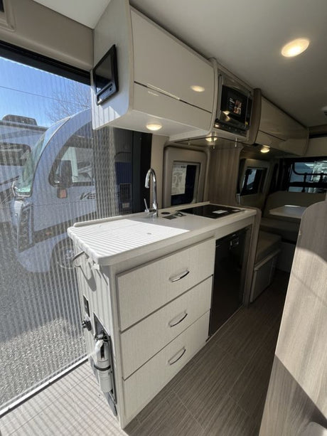 Modern RV rental interior features a compact kitchen with sink, stovetop, microwave, fridge, and ample storage.