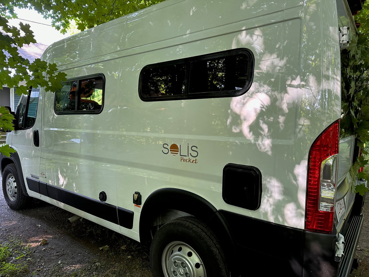  and a large window looking out to nature.|White Solis Pocket camper van RV rental with extended yellow awning on gravel. Perfect for outdoor adventures.|A white Winnebago camper van — photo 20