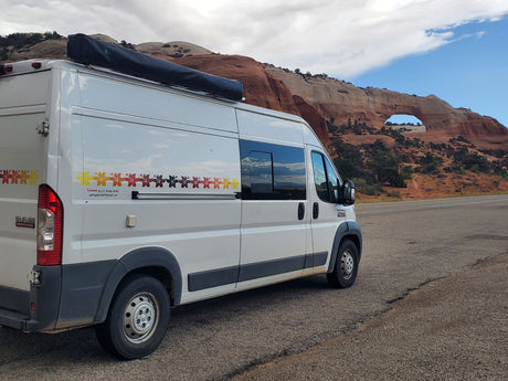 Scenic RV rental: A white camper van beside a natural rock arch and red rock formations.