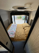 Inside a cozy RV rental: a comfortable bed, overhead AC, and a view through the open rear. A compact mobile living space.