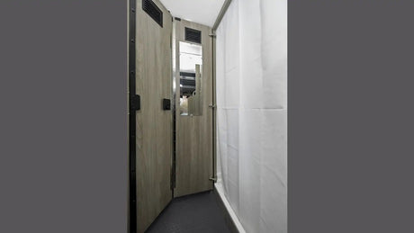 View inside an **RV rental** bathroom: features wood-look door with mirror, and white shower curtain for a compact **shower** area.
