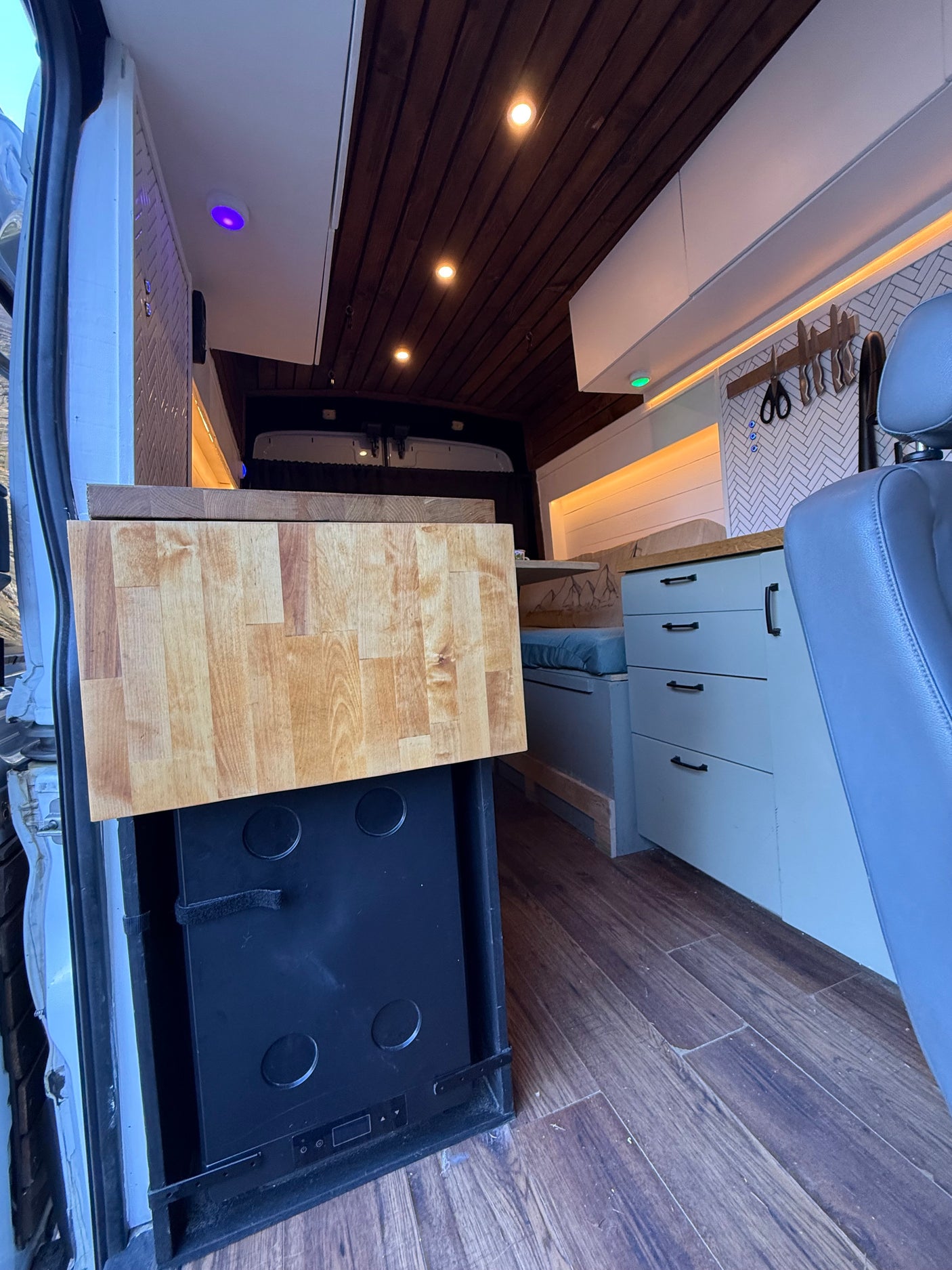 RV rental kitchen setup featuring a pull-out countertop, hidden fridge, custom cabinets, wood ceiling, and comfy seating.