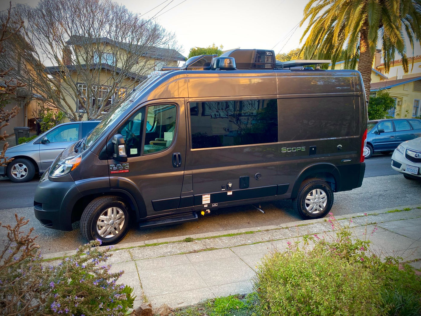 Side view of a grey Ram ProMaster RV rental, a compact camper van ideal for road trips, parked on a sunny street.