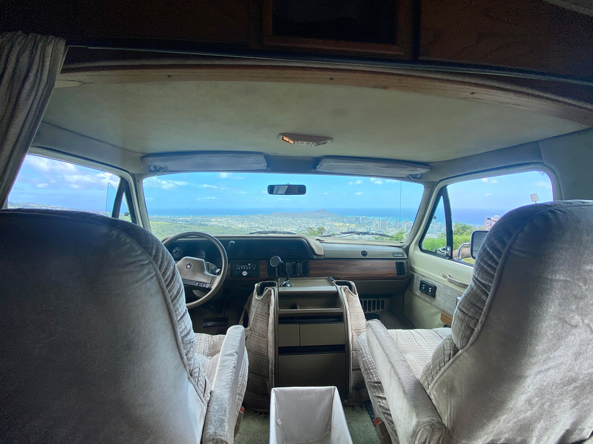 Inside an RV rental showing the front seats, dashboard, and a stunning panoramic view of a Hawaiian city, ocean, and Diamond Head. — photo 6