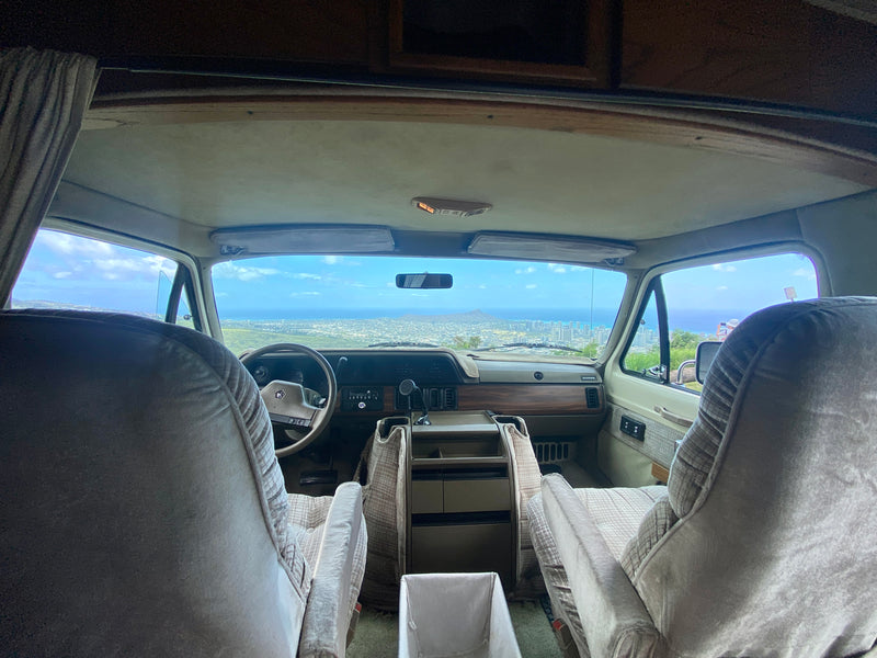 Inside an RV rental showing the front seats, dashboard, and a stunning panoramic view of a Hawaiian city, ocean, and Diamond Head. — photo 6