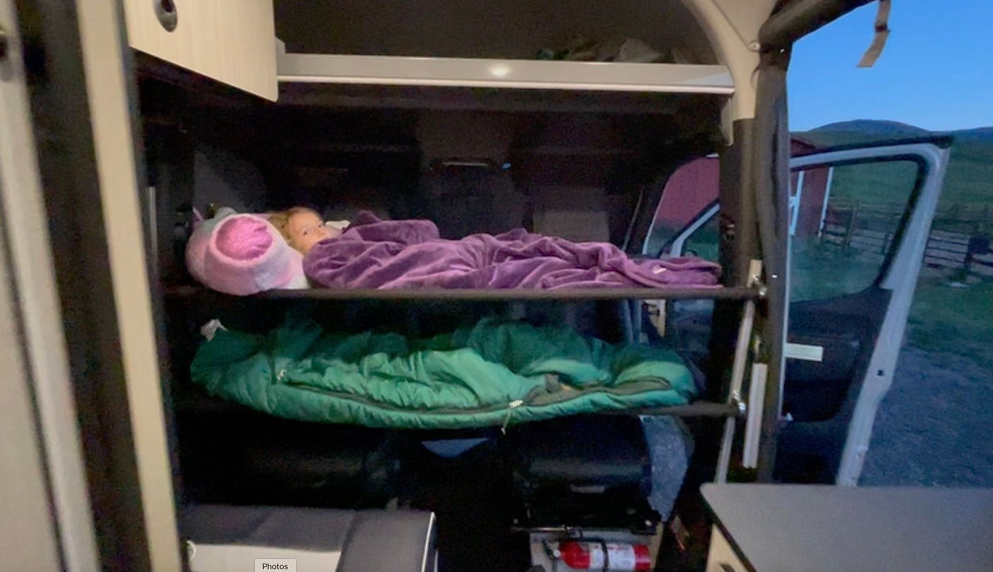 Cozy RV rental adventure: A child sleeps on an upper bunk inside a camper van, with a lower bunk and outdoor view visible. — photo 11