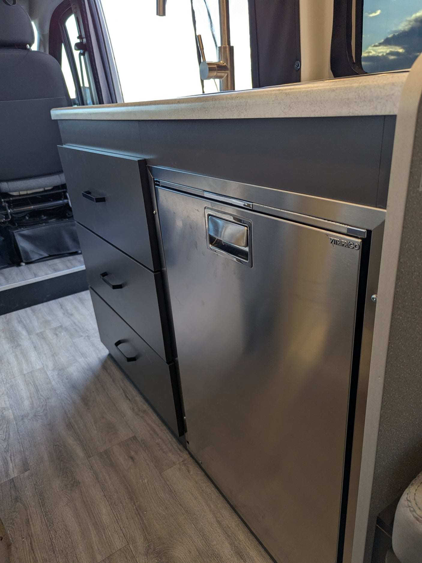 Modern RV rental interior with compact kitchen: countertop, faucet, drawers, and built-in fridge.