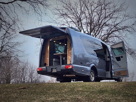 This gray custom camper van, perfect for rv rental, reveals its cozy, lit interior with open rear hatch & side door on a grassy hill.