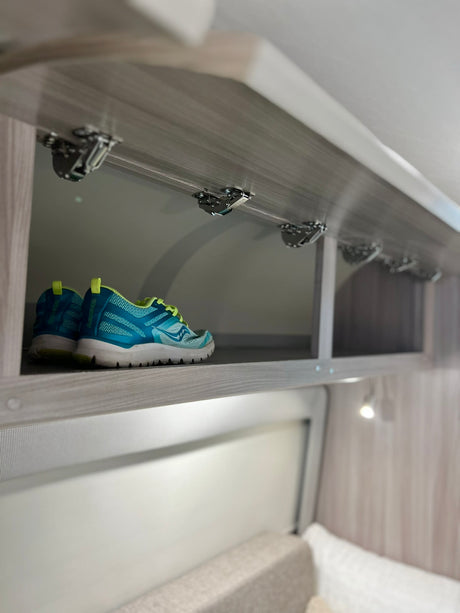 RV rental storage: Blue sneakers neatly stored in an overhead cabinet, showing efficient interior design.