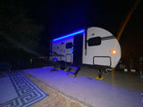RV rental at night, illuminated by striking blue LED awning lights, offering a cozy and stylish camping setup.