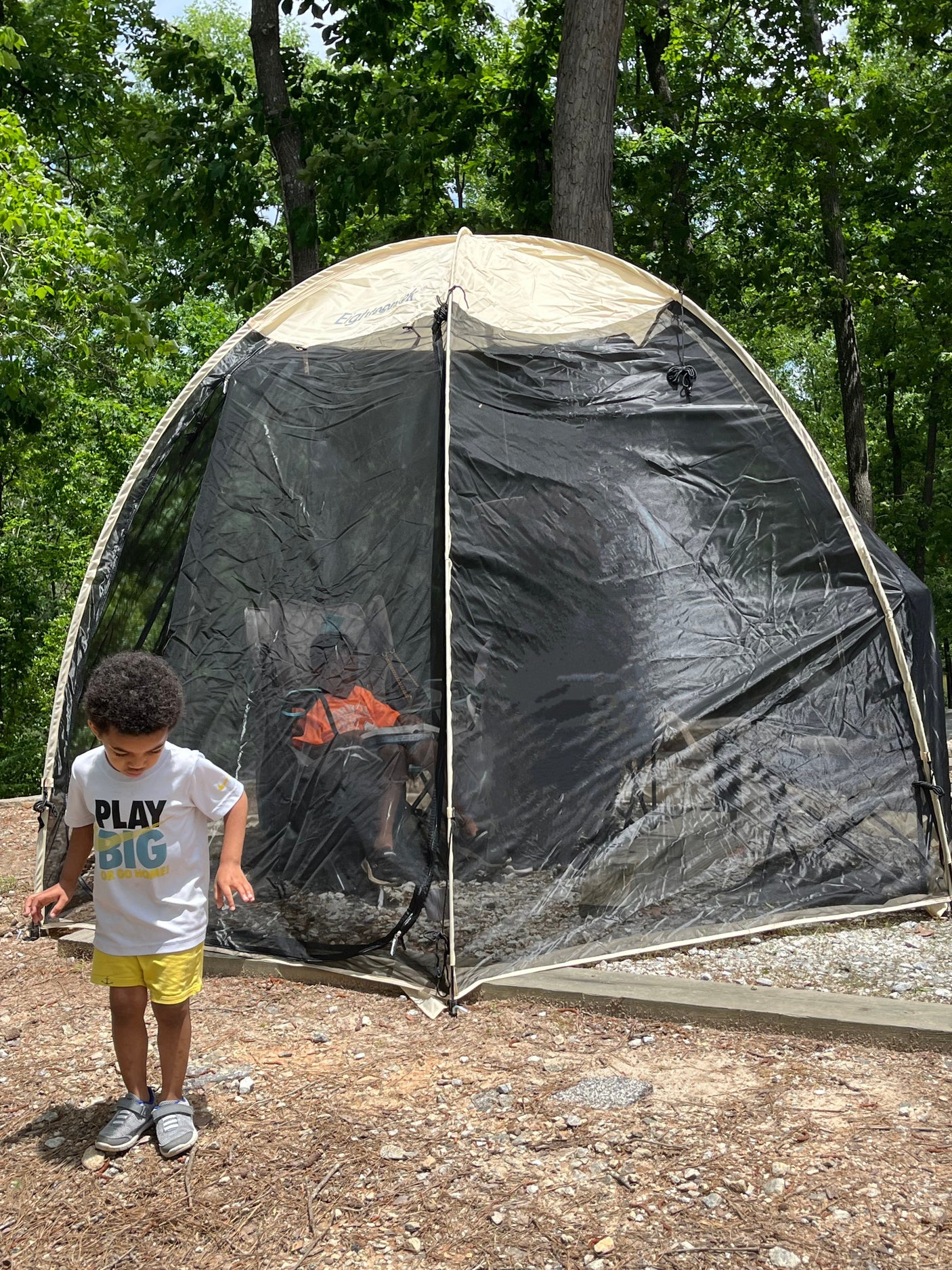 Boy at an RV rental campsite. A screen room provides shaded space, with a person visible inside enjoying the outdoors.
