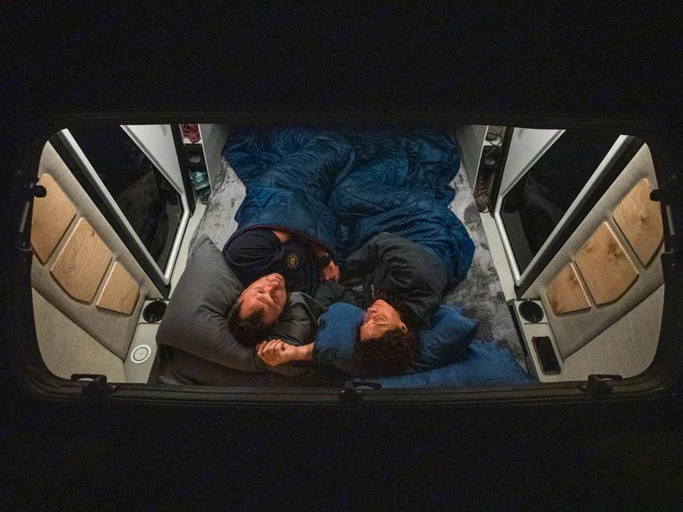 RV rental: Overhead view of a couple sleeping soundly in a cozy camper van bed. Perfect comfort for travel adventures.