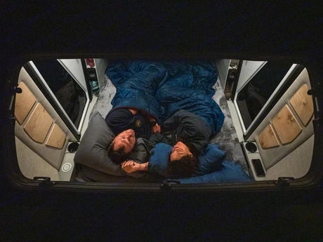RV rental: Overhead view of a couple sleeping soundly in a cozy camper van bed. Perfect comfort for travel adventures.