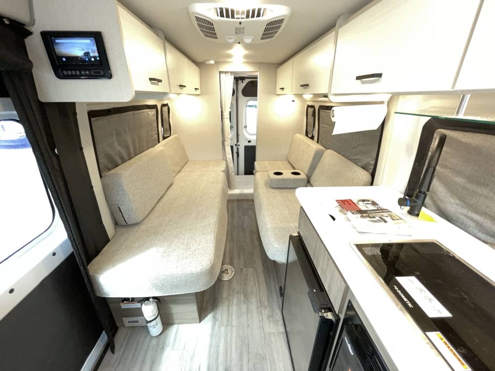 Modern RV rental interior showing a comfortable living space with facing sofas and a compact kitchen.