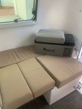 This RV rental's interior features an Alpicool portable fridge and versatile beige seating next to a window.