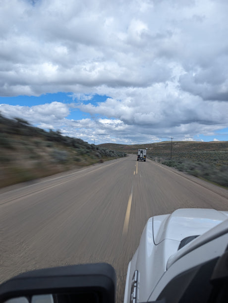 Scenic road trip: Following a truck camper on a wide road under partly cloudy skies. Great for rv rental travel!